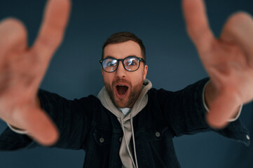 Naklejka premium Guy is pretending that he's doing photoshoot by using hands gestures. Handsome man is in the studio against blue background