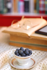 Plate of cookies, cup of tea, fresh blueberries, dry oranges, stack of books, reading glasses and tablet on the table. Hygge at home. Selective focus.