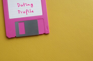 Pink floppy Disk on yellow copy space background with handwritten text DATING PROFILE - short...