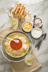 Orange Keta Lachs Kaviar in Dose auf Eis in Glas Schale mit Perlmutt Löffel, Sekt Champagner, gekochte Eier Würfel, Charlotten Zwiebel Würfel, Toast Brot und Saure Sahne auf Serviette und Marmor hell