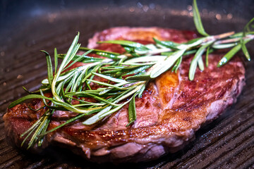 Juicy beef steak frying on a pan with rosemary. Closeup