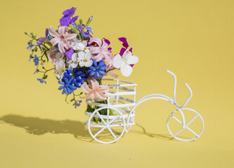souvenir bicycle carries spring bouquet of various flowers in basket on yellow background. Birthday...