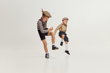 Fototapeta na wymiar Active boys, children in stylish classical clothes playing together, running, jumping over grey studio background. Fun. Concept of game, childhood, friendship