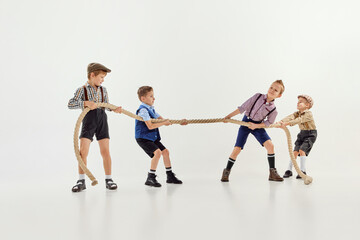 Fototapeta na wymiar Competition. Group of little boys, children playing together, pulling the rope over grey studio background. Concept of game, childhood, friendship
