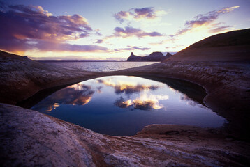 A depression in the rock holds rainwater that mirrors the western sky in Lake Powell, Utah.