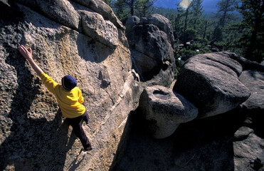 Wide angle of a young male rock climber bouldering on granite.