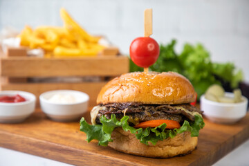 Homemade hamburger served with french fries. It looks delicious prepared with onions, hamburger patties, cheddar cheese and ham.