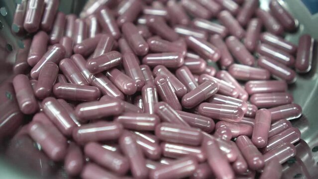 recopilaci&oacute;n de c&aacute;psulas, p&iacute;ldoras, pastillas de color rosado por maquina industrial de empresa farmac&eacute;utica.