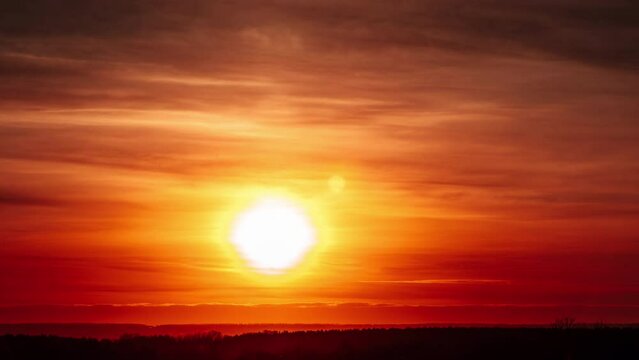 Timelapse of sunset with a lens flare in the orange sky with soft clouds over the horizon. Big bright red sun with sunrays moves down. Awesome epic cloud space, vibrant color. Time Lapse. Sundown