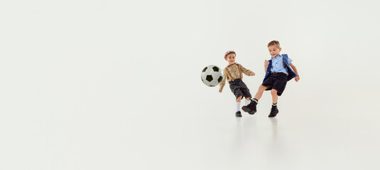 Fototapeta na wymiar Dribbling. Boys, children in classical retro clothes playing football over grey studio background. Banner, flyer. Concept of game, childhood, friendship