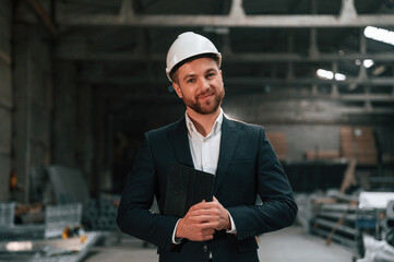 Positive manager in black formal wear at the factory. Standing and smiling