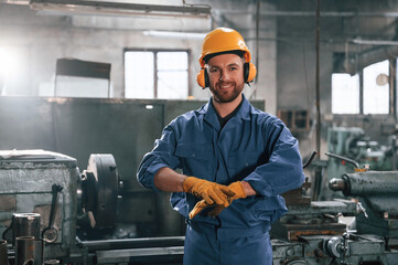 In hearing protection earphones. Factory worker in blue uniform is indoors