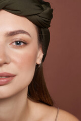 Cropped portrait of a lady in a hairband and a shiny silver earring made as a drop. The pretty girl is wearing a minimalistic silvery drop earring and posing on the brown background.