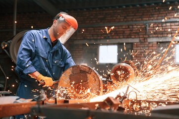 In protective shield on head. Welding the metal. Factory worker in blue uniform is indoors