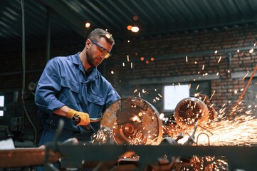 Welding the metal. Factory worker in blue uniform is indoors
