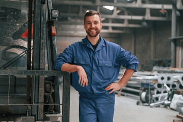 Fototapeta na wymiar With the forklift. Factory worker in blue uniform is indoors