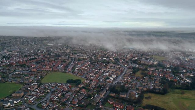 Urban Sprawl showing a small industrial UK town. Urban aerial scene. Drone footage. Showing drifting low clouds busy streets, urban housing and industrial plants, factories. Typical UK townscape.