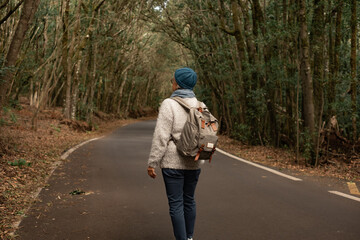 Back view of mature  woman enjoying freedom in outdoors walking in a mountain road. Elderly active woman traveling  in a forest holding backpack enjoying nature and vacation