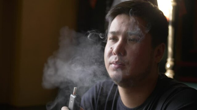 Portrait of a man smoking a tobacco heating device at a table by the window in a cafe. Close-up of a sad guy sitting with an electronic cigarette in his hand.