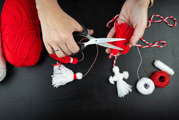 Woman making handmade traditional martisor, from red and white strings with tassel. Symbol of...