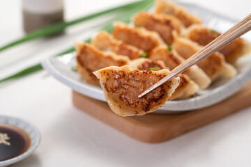 Pan-fried gyoza dumpling jiaozi in a plate with soy sauce on white table background.