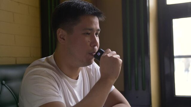 Portrait of a man smoking a tobacco heating device at a table by the window in a cafe. Close-up of a sad guy smoking an electronic cigarette.