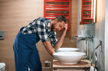 Can't fix the crane. Plumber in blue uniform is at work in the bathroom