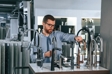 A large selection of water faucets. Man chooses a products in a sanitary ware store