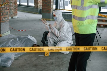 Woman is putting on the gloves. Detectives are collecting evidence in a crime scene near dead body