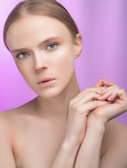 Beauty and skin care. Happy woman with fresh radiant, moisturized skin, standing with bare shoulders, with light makeup and natural skin on a pink background.