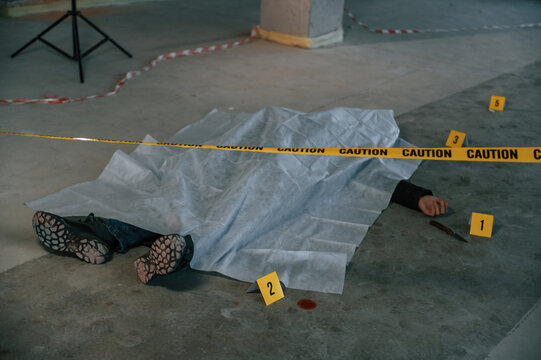 Knife and blood. Dead body of a man is on the ground, covered in white cloth. Conception of murder, homicide