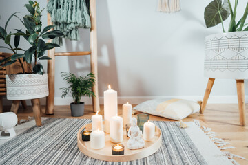 Wooden tray with burning candles and white Buddha statuette on the floor of modern Scandi interior. Zen Composition for meditation, yoga practice, relaxation. Balance and calm energy flow indoor