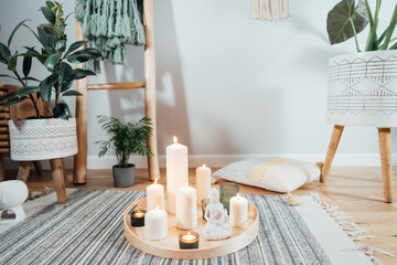 Wooden tray with burning candles and white Buddha statuette on the floor of modern Scandi interior....