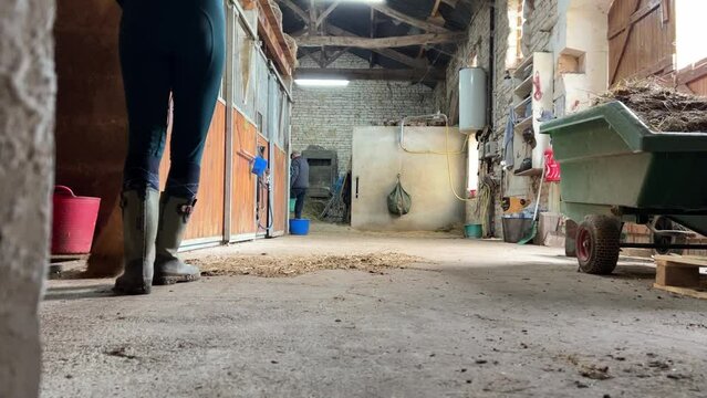 Girl in wellington boots sweeping the stable floors