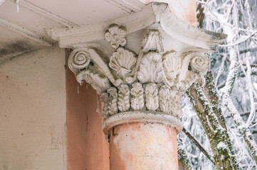 An architectural ancient structure with columns and stucco. The building is made in the antique style. A building with pink columns in a park with snow-covered trees. An old building with columns.