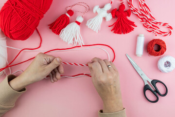 Woman making handmade traditional martisor, from red and white strings with tassel. Symbol of holiday 1 March, Martenitsa, Baba Marta, beginning of spring in Romania, Bulgaria, Moldova