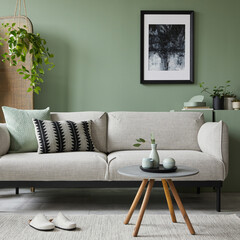 Stylish composition of modern living room interior. Mock up poster frame, modern sofa, folding screen, plants and personal accessories. Sage green wall. Home staging. Template. Copy space.