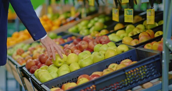 man customer choosing ripe apples from shelf in supermarket, closeup view, 4K, Prores