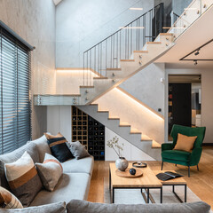 Stylish composition of stairs in living room interior. Grey sofa, green velvet armchair, coffee...