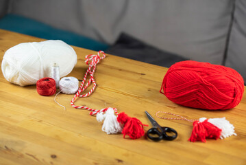Woman making handmade traditional martisor, from red and white strings with tassel. Symbol of...