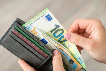 Female hands with grey wallet full of euro money, taking some bills out. Woman making a purchase,...