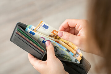 Woman holding her wallet with euro banknotes and counting them. Purchasing, buying goods, business and wealth concept - obrazy, fototapety, plakaty