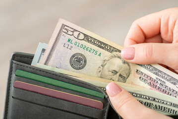 American fifty dollar banknote and grey wallet in female hands, close up. Finances, US money, world...