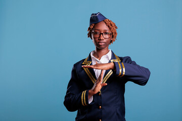 Tired female flight attendant gesturing time out and pause in studio against blue background....