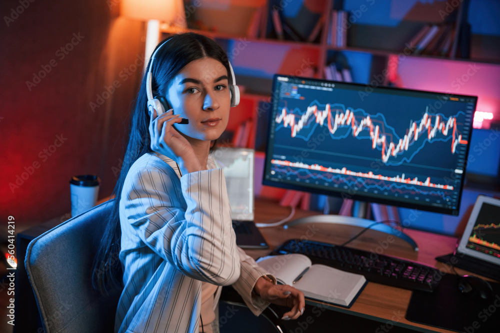 Poster looking into the camera. female stock trader is working by pc indoors. conception of exchange and mo