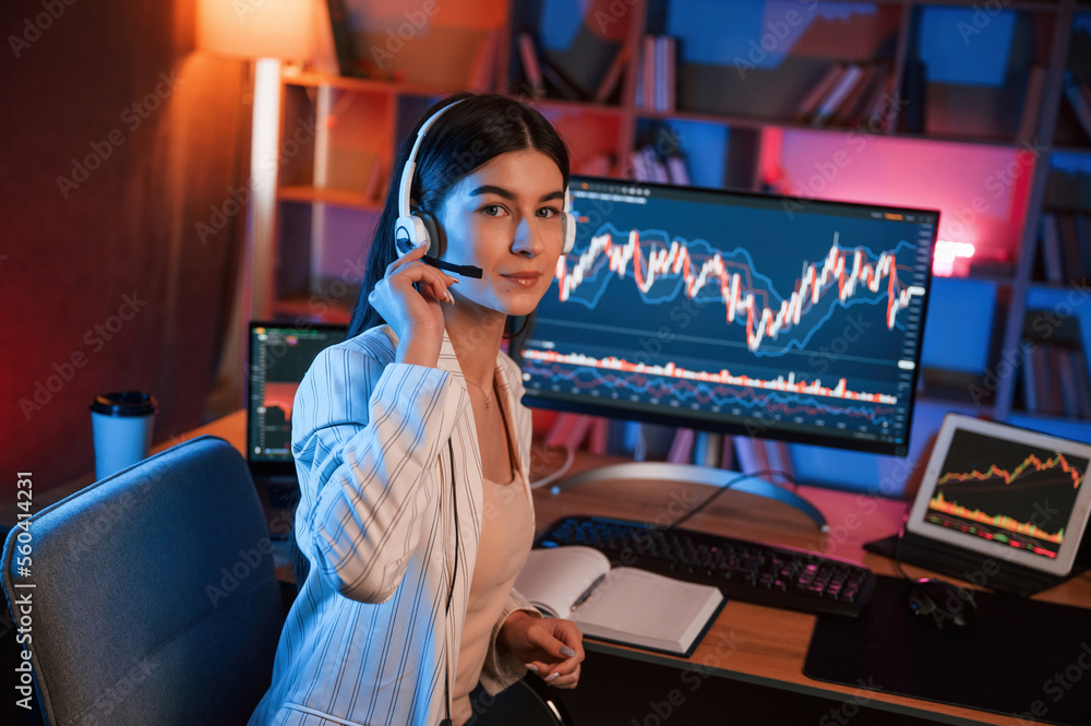 Poster looking into the camera. female stock trader is working by pc indoors. conception of exchange and mo