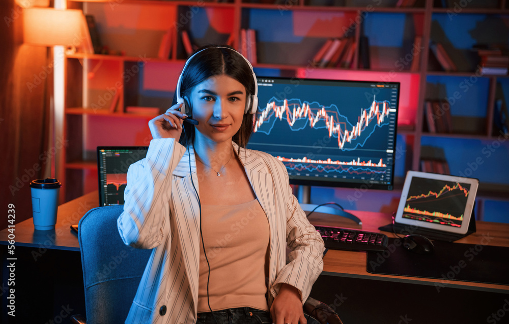 Poster looking into the camera. female stock trader is working by pc indoors. conception of exchange and mo