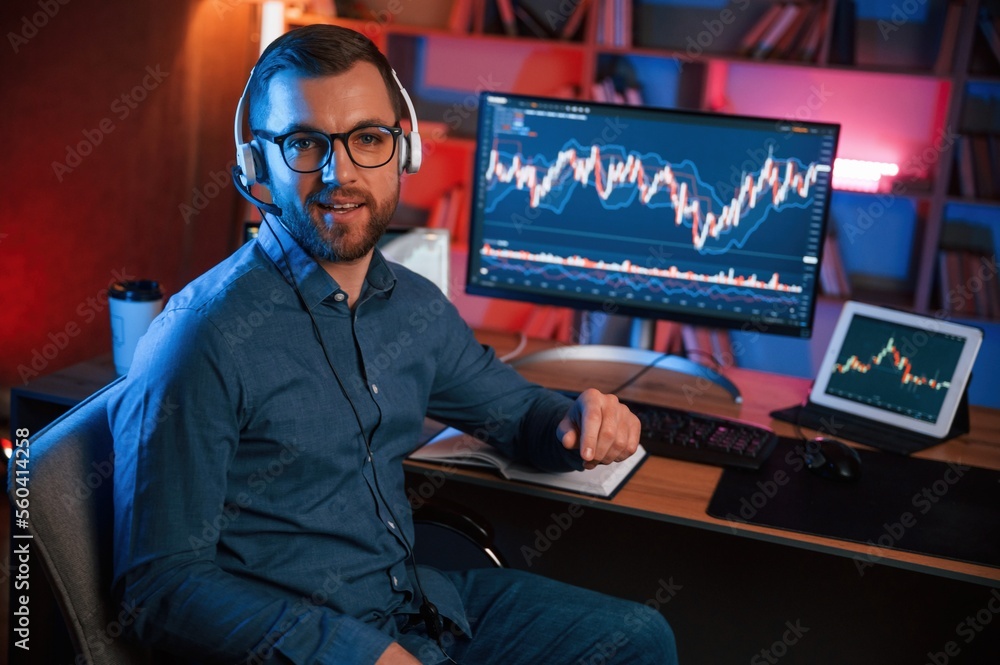 Poster sitting and looking at the camera. stock trader is working by pc indoors. conception of exchange and
