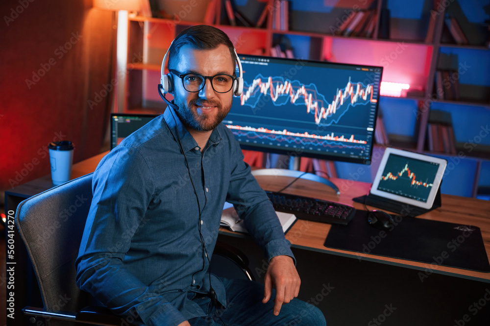 Poster sitting and looking at the camera. stock trader is working by pc indoors. conception of exchange and