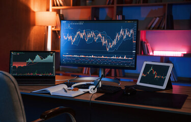 Computer with stock exchange graph on display is in the dark room with neon lighting